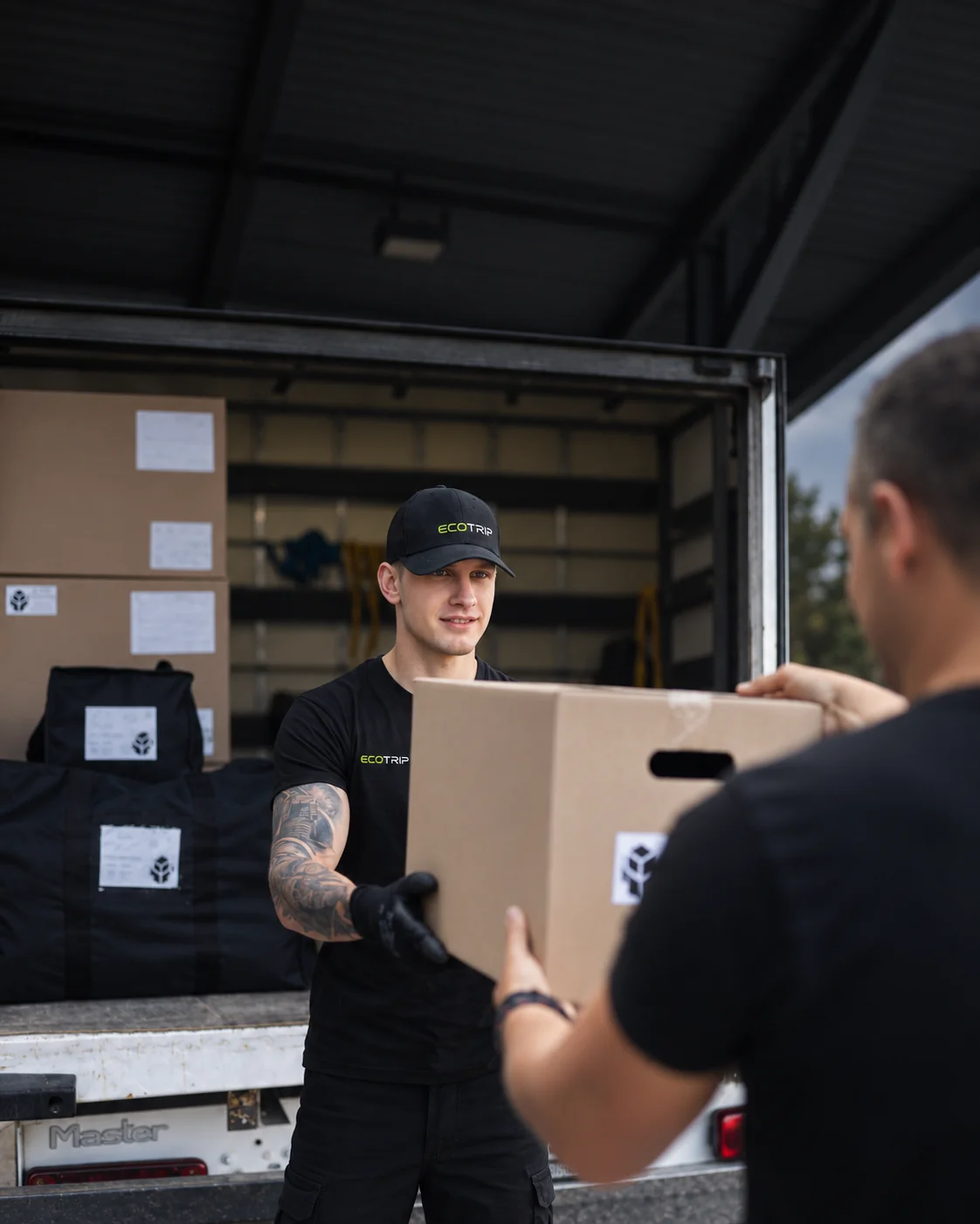 An EcoTrip staff member handing a packed box to another person beside a vehicle. Illustration.