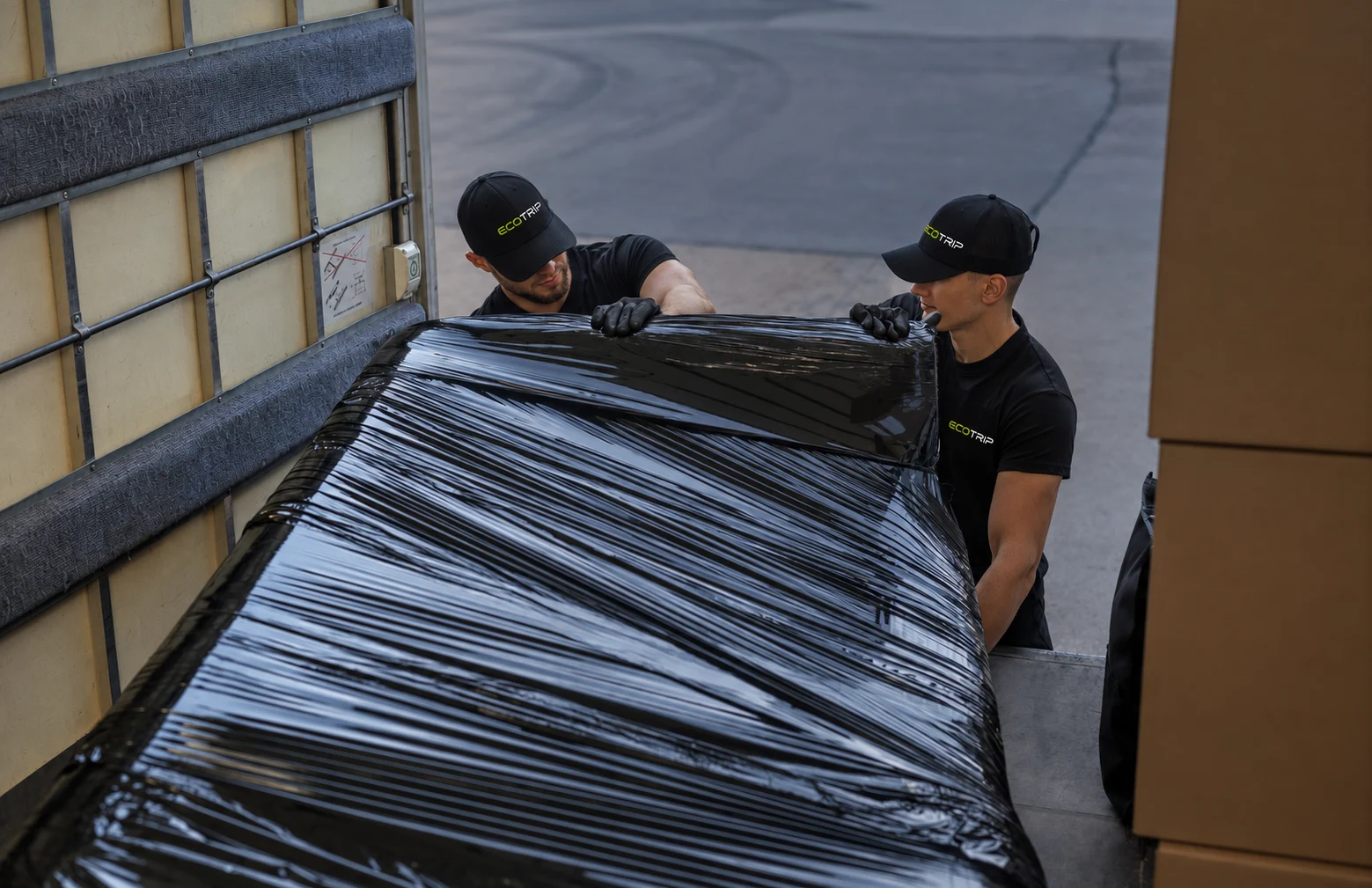 Two EcoTrip staff loading a piece of furniture wrapped in protective film into a vehicle. Illustration.